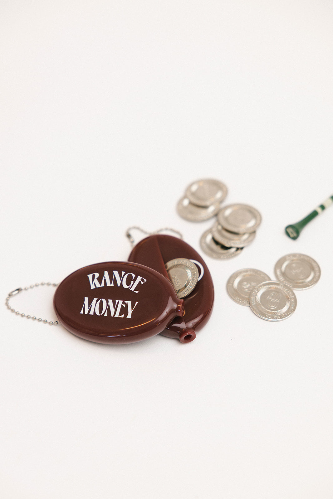 Brown case with 'Range Money' text, silver coins, and a green tee on a white background