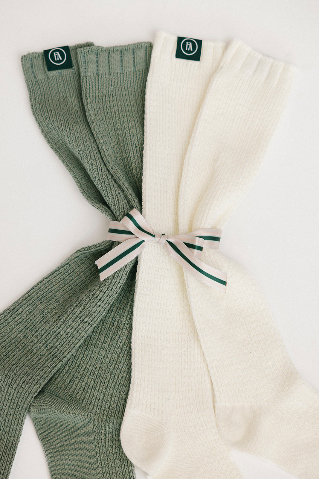 Two pairs of ribbed knee-high socks, one green and one white, tied together on a light background.