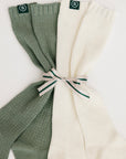 Two pairs of ribbed knee-high socks, one green and one white, tied together on a light background.