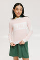 A woman wearing a pink fore all Fore Sweater with white accents and a green skirt.