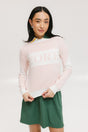A woman wearing a pink fore all Fore Sweater with white accents and a green skirt.