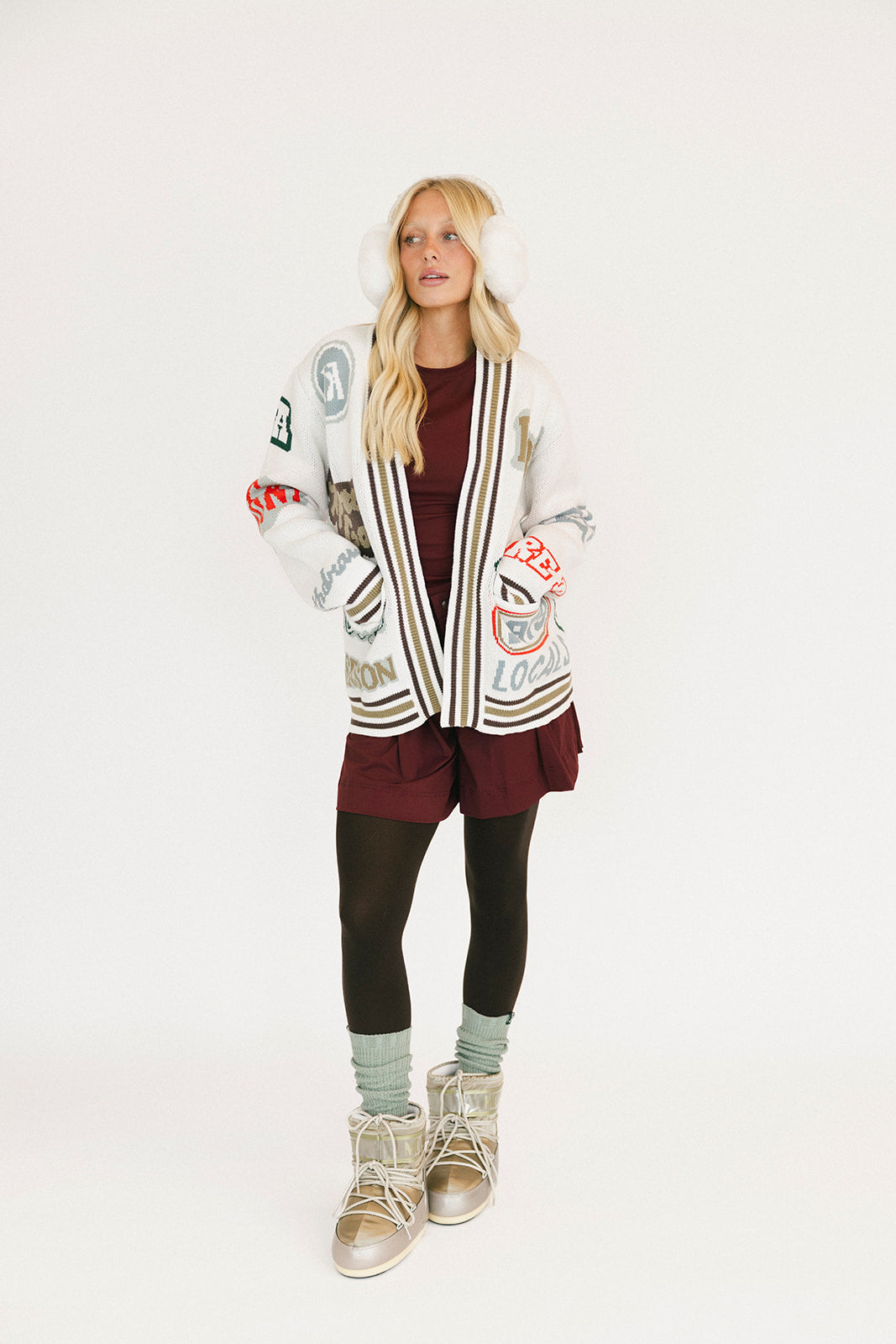 Person wearing a patterned cardigan, maroon dress, and black leggings on a white background