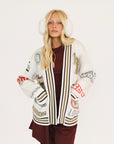 Woman wearing a patterned cardigan with white ear muffs on a white background