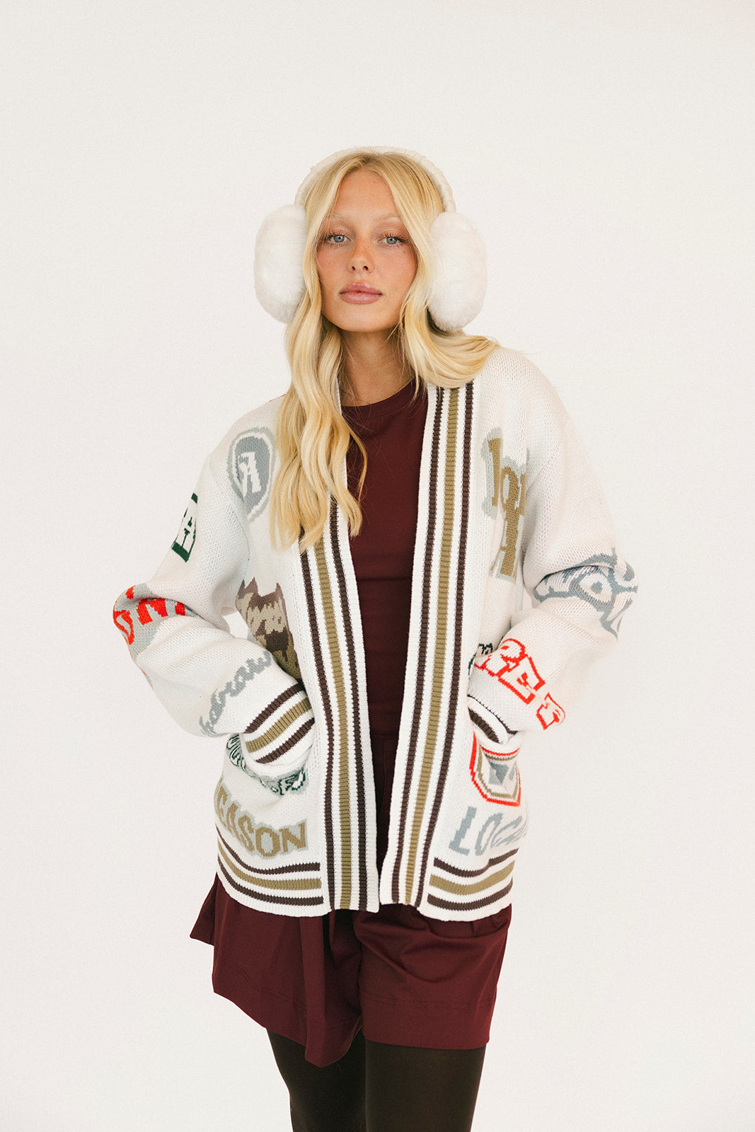 Woman wearing a patterned cardigan with white ear muffs on a white background
