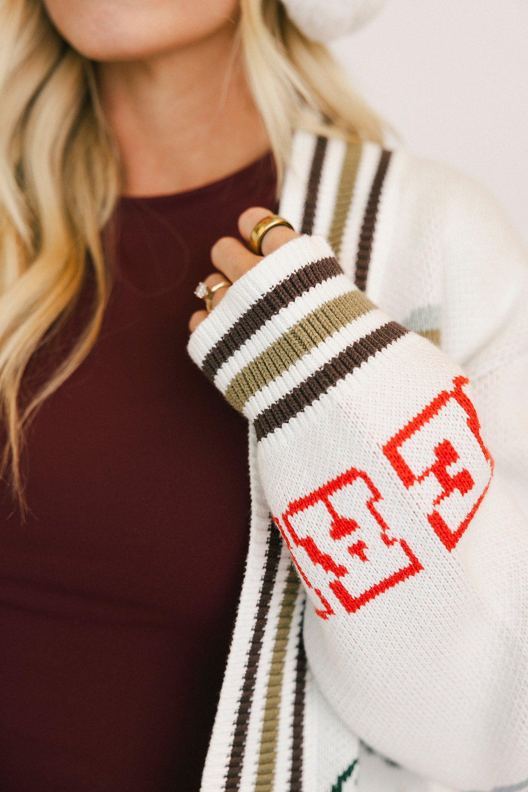 Close-up of a person wearing a white knit sweater with red and black patterns, held against a blurred background.