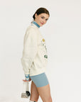 Person wearing a white sweater with graphic design and text, standing against a plain background
