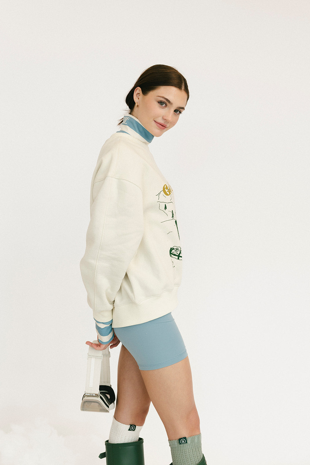 Person wearing a white sweater with graphic design and text, standing against a plain background