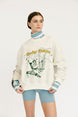 Person wearing a white sweater with graphic design and text, standing against a plain background