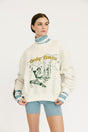 Person wearing a white sweater with graphic design and text, standing against a plain background
