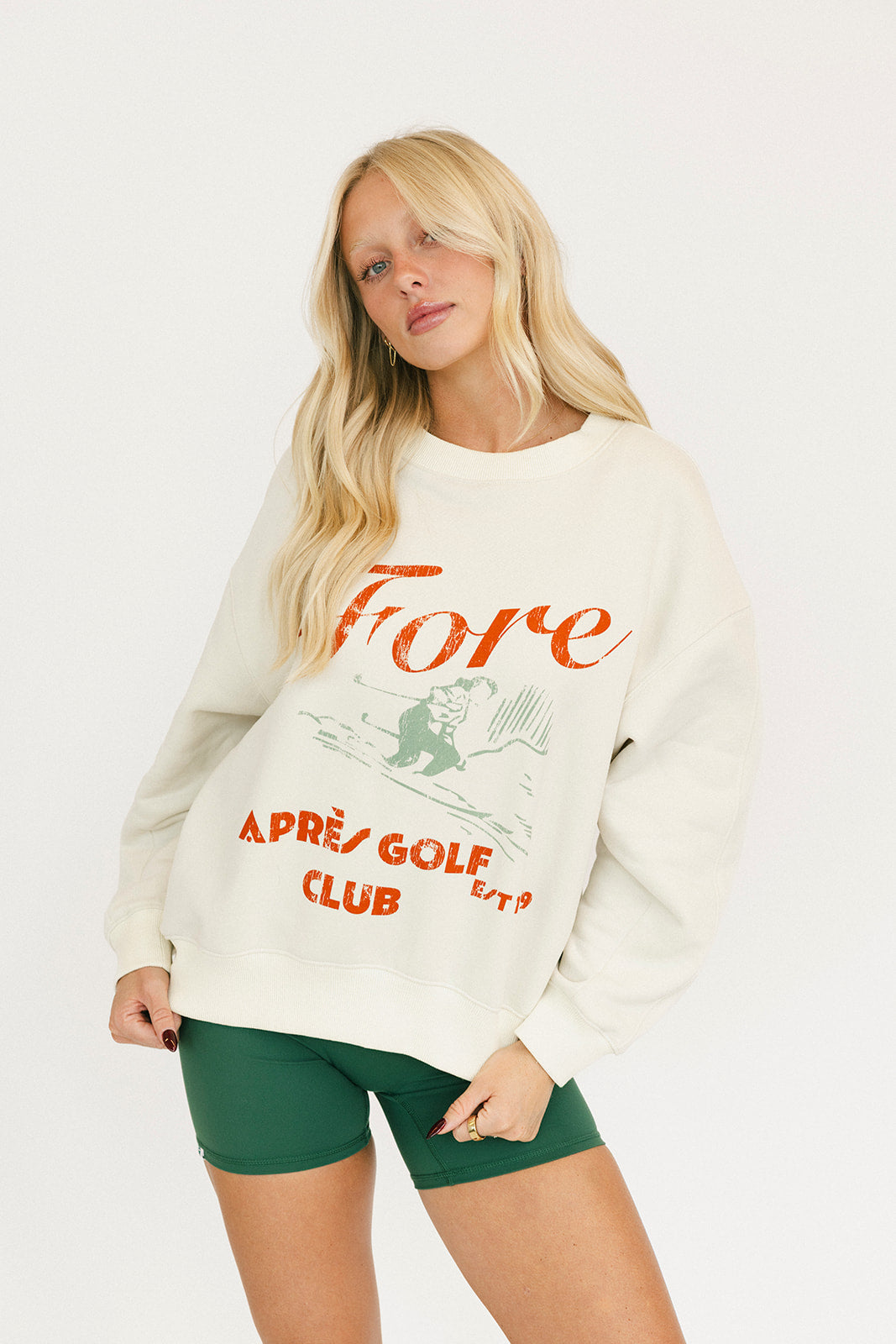 Woman wearing a white sweatshirt with red text and green shorts on a white background