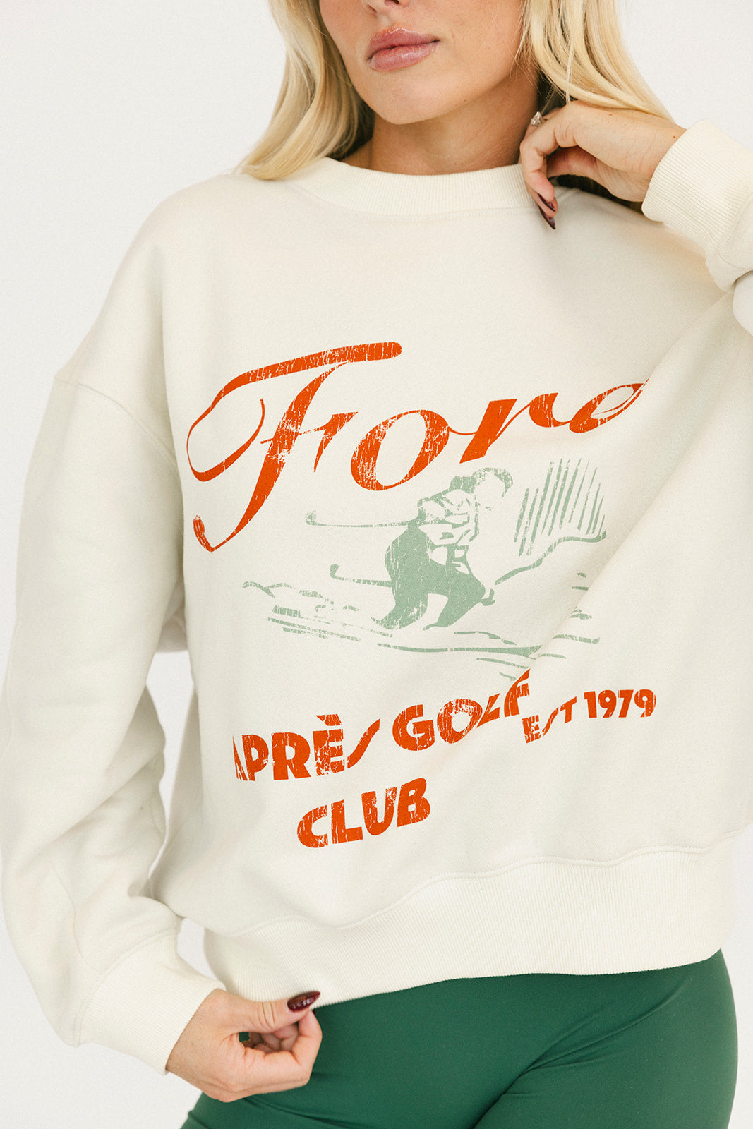 Person wearing a cream sweatshirt with red and green text and graphics.