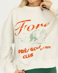 Person wearing a cream sweatshirt with red and green text and graphics.
