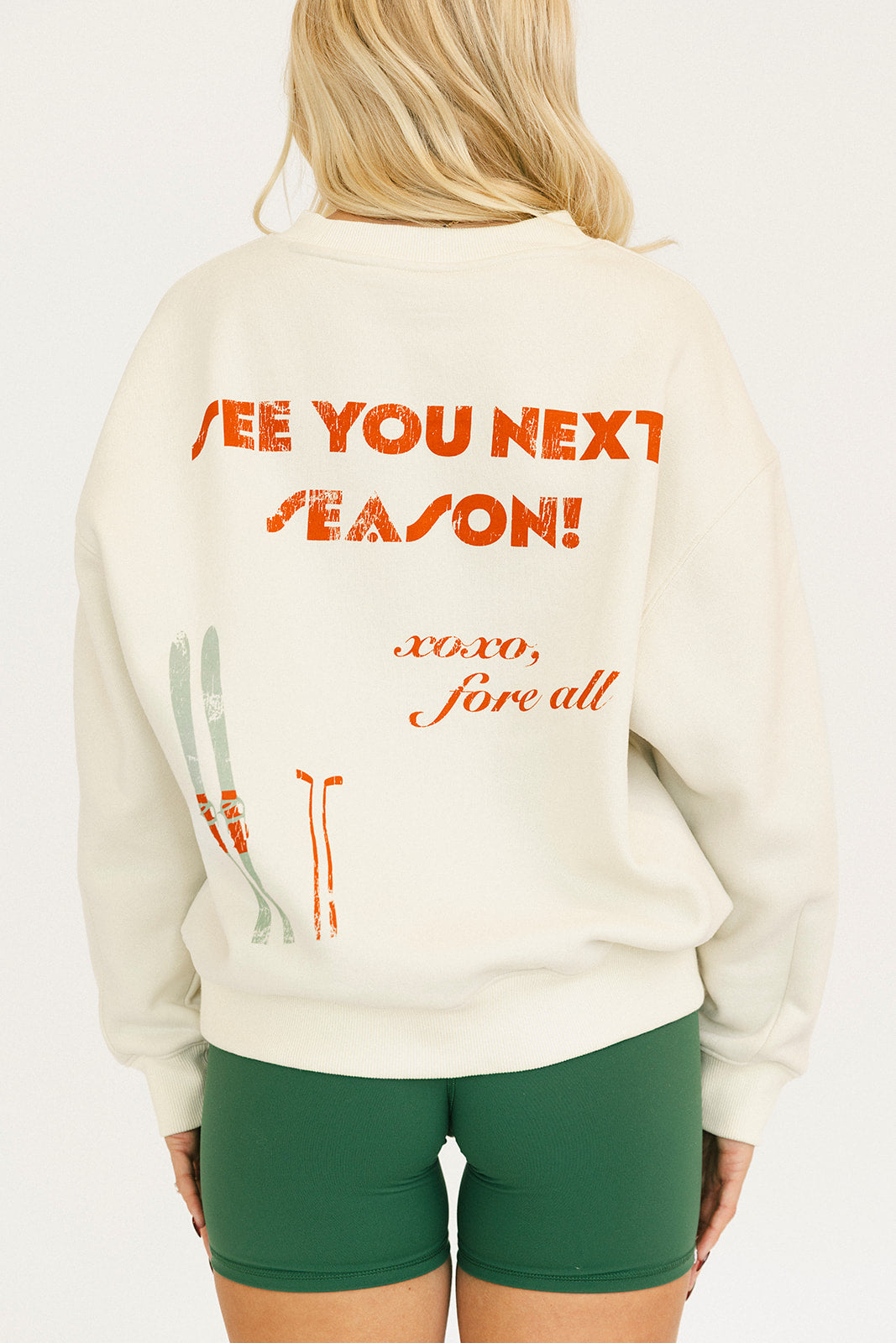 Woman wearing a white sweatshirt with red text and green shorts on a white background