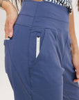 A female model wearing a sleeveless top with a geometric pattern and blue athletic pants, standing against a white background.