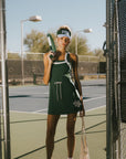 Woman in a green dress holding tennis rackets on a tennis court