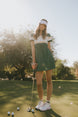Woman on a golf course holding a golf club with trees in the background