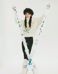 Person wearing a white sweater with text and black pants, standing against a white background.