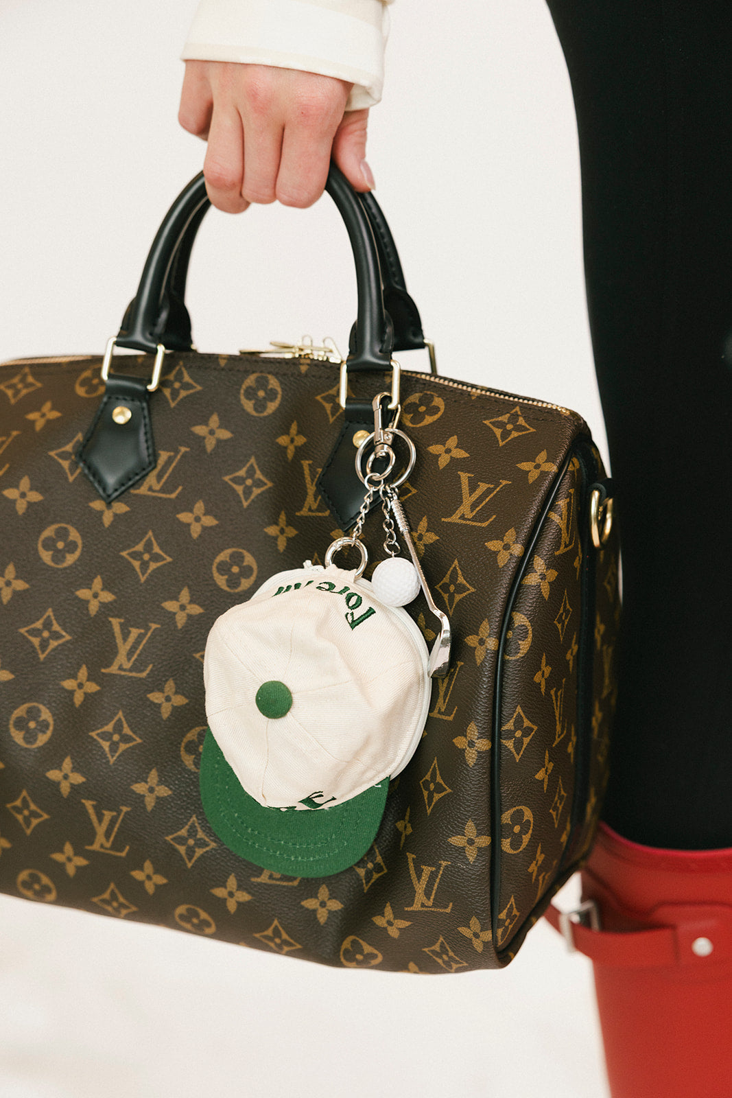 Louis Vuitton handbag with a unique keychain held by a person wearing red boots.