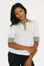 stylish women’s golf top outfit. Woman wearing a white blouse with green patterned accents on a plain background