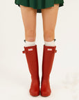 Red rain boots with a brand logo worn by a person on a white background