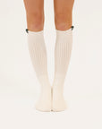 White knee-high socks worn by a person on a light beige background