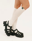 Black sandals worn with white knee-high socks on a white background
