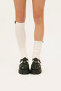 Person wearing white knee-high socks and black shoes on a white background