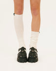 Person wearing white knee-high socks and black shoes on a white background