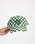 Green and white checkered cap held by a hand on a white background