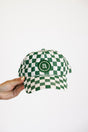 Green and white checkered cap held by a hand on a white background