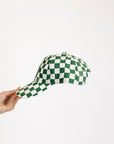 Green and white checkered cap held by a hand on a white background