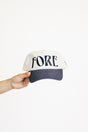 Cap with 'FORE' text held by a hand on a white background