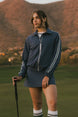 Woman in a blue tracksuit standing on a golf course with mountains in the background
