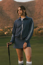 Woman in a blue tracksuit standing on a golf course with mountains in the background