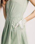 Person wearing a light green dress with a white glove on a plain background