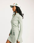 Woman wearing a light green long-sleeve top and skirt with a matching cap on a white background