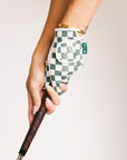 Hand wearing a green and white checkered glove holding a golf club on a plain background