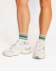 White sneakers with green accents worn by a person on a white background