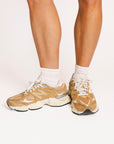Person wearing pink and white striped socks and tan sneakers with white laces on a plain background