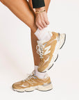 Person wearing pink and white striped socks and tan sneakers with white laces on a plain background