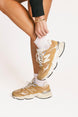 Person wearing pink and white striped socks and tan sneakers with white laces on a plain background