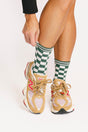 Person wearing green checkered socks with beige sneakers on a white background