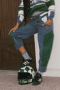 A pair of indigo and green color-blocked warm-up pants with a flat drawstring waistband, deep front pockets, and a barrel style fit. The pants feature appliqué logos, including the 'Fore All' detail on the back and an FA icon on the inner calf.