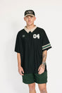 Person wearing a black sports jersey with white lettering and green shorts on a white background