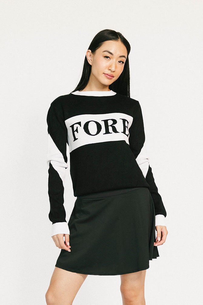 Woman wearing a black and white sweater with 'FORE' text, black skirt, and black boots on a white background