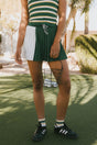 Person wearing a green and white striped top with a green skirt and black Adidas shoes in an outdoor setting.