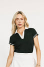 Woman wearing a black polo shirt, white skirt, and sneakers on a white background