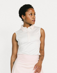 Woman wearing a white sleeveless Moore Polo and light pink skirt on a white background