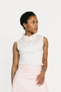 Woman wearing a white sleeveless Moore Polo and light pink skirt on a white background