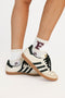 White sneakers with black stripes and 'F' logo worn with white socks on a light background
